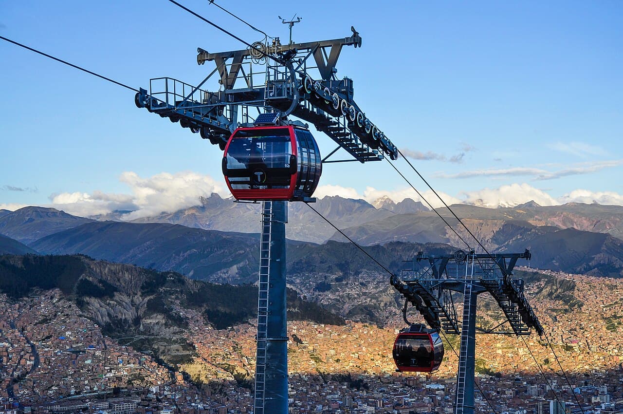 Red cable cars gliding over the rooftops of La Paz with snowy Mount Illimani in the background