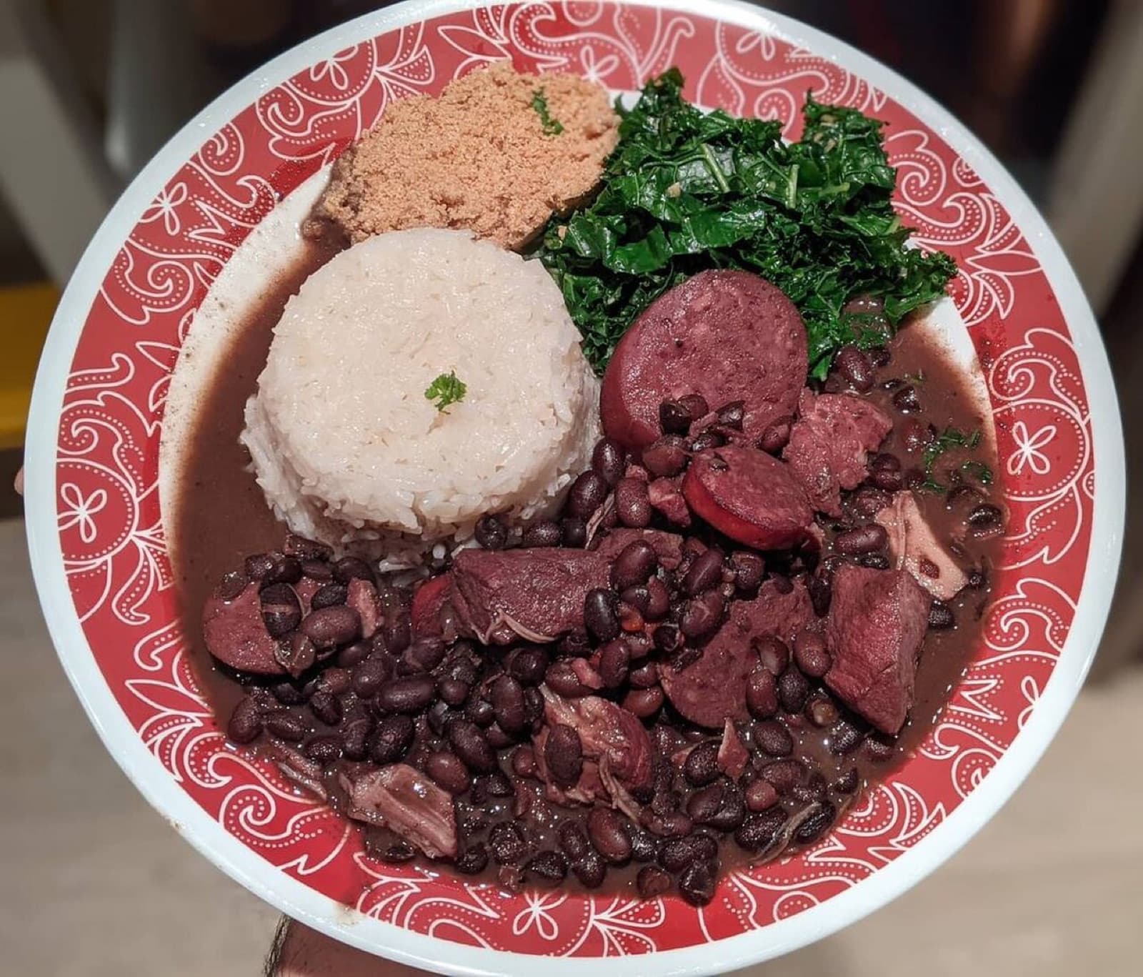 A bowl of feijoada with black beans, rice, greens and farofa