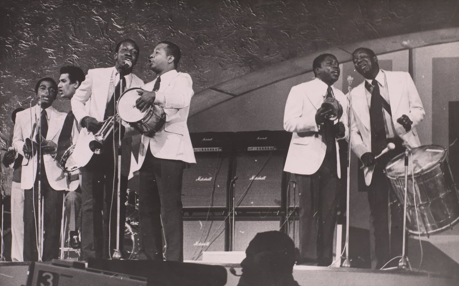 A samba group performing on stage with drums and microphones