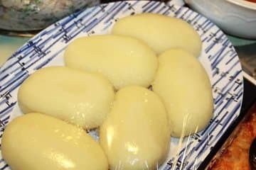 A smooth ball of foutou beside a bowl of thick orange-brown peanut sauce