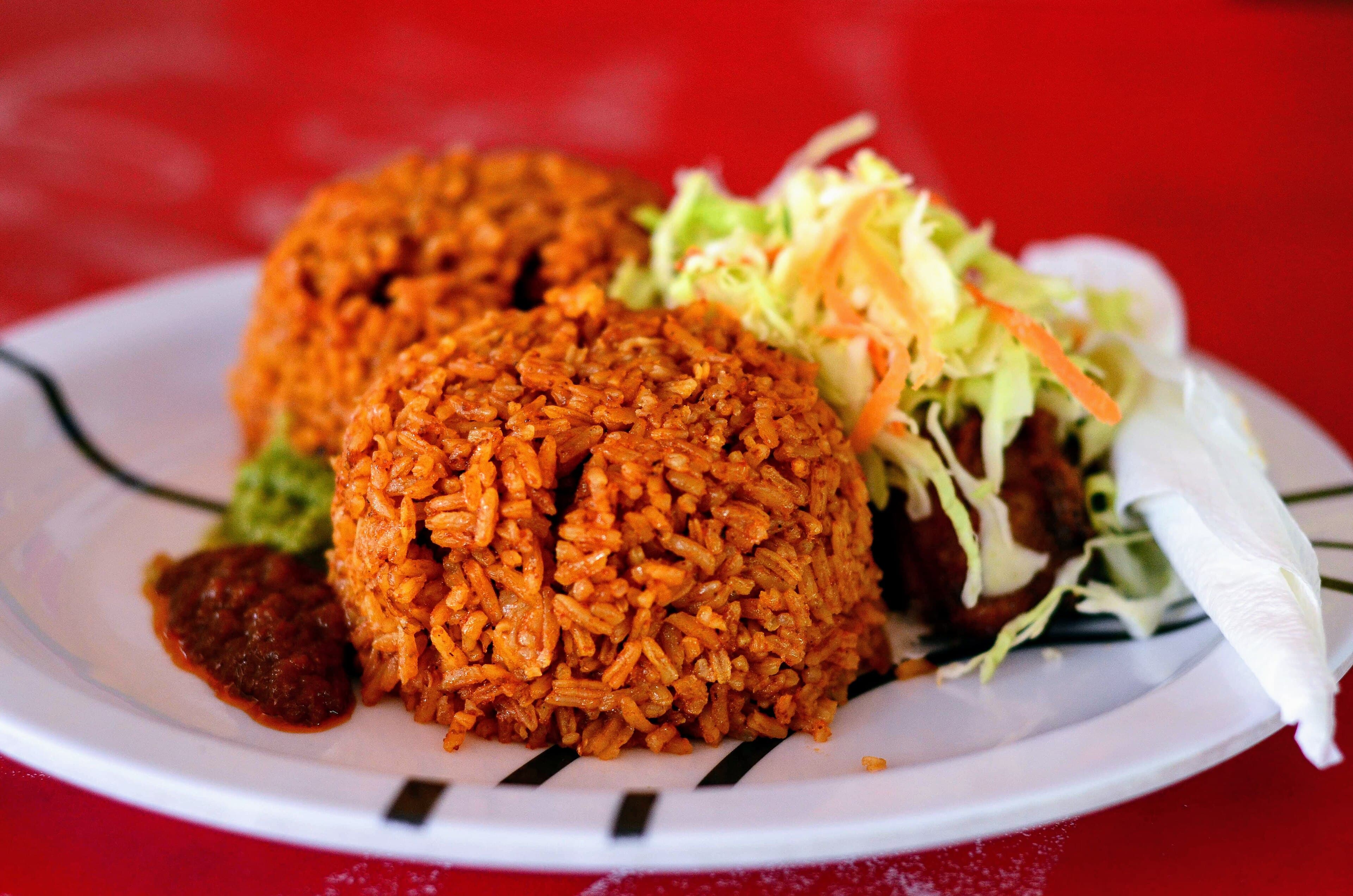 A large pot of bright orange-red jollof rice with vegetables and fish on top