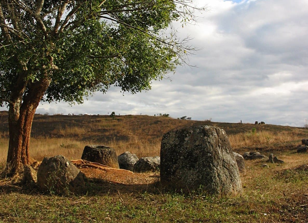 Large ancient stone jars scattered across a green hillside on the Plain of Jars in Laos