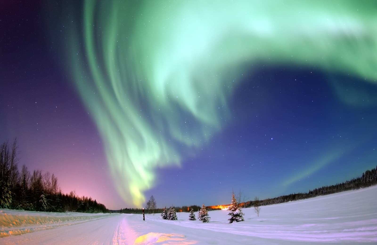 Green and pink aurora borealis swirling above a snowy Norwegian landscape