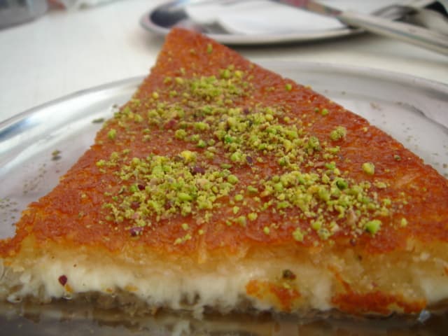 A large round tray of knafeh - golden shredded pastry with white cheese and orange syrup