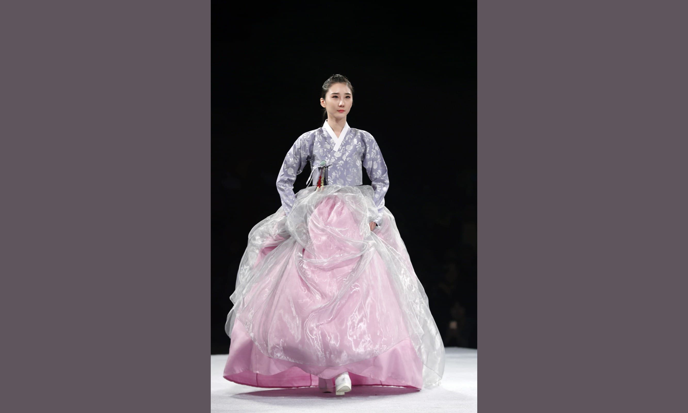 A model wearing a hanbok with a purple top and pink and silver skirt