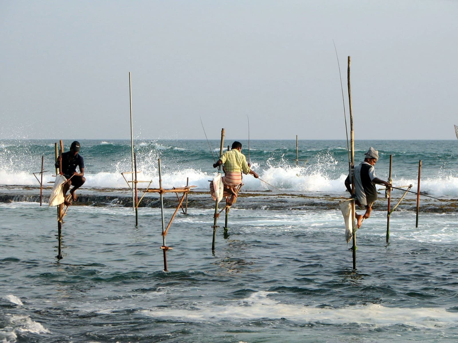 Three stilt fishermen perched on poles in the surf near Unawatuna, Sri Lanka