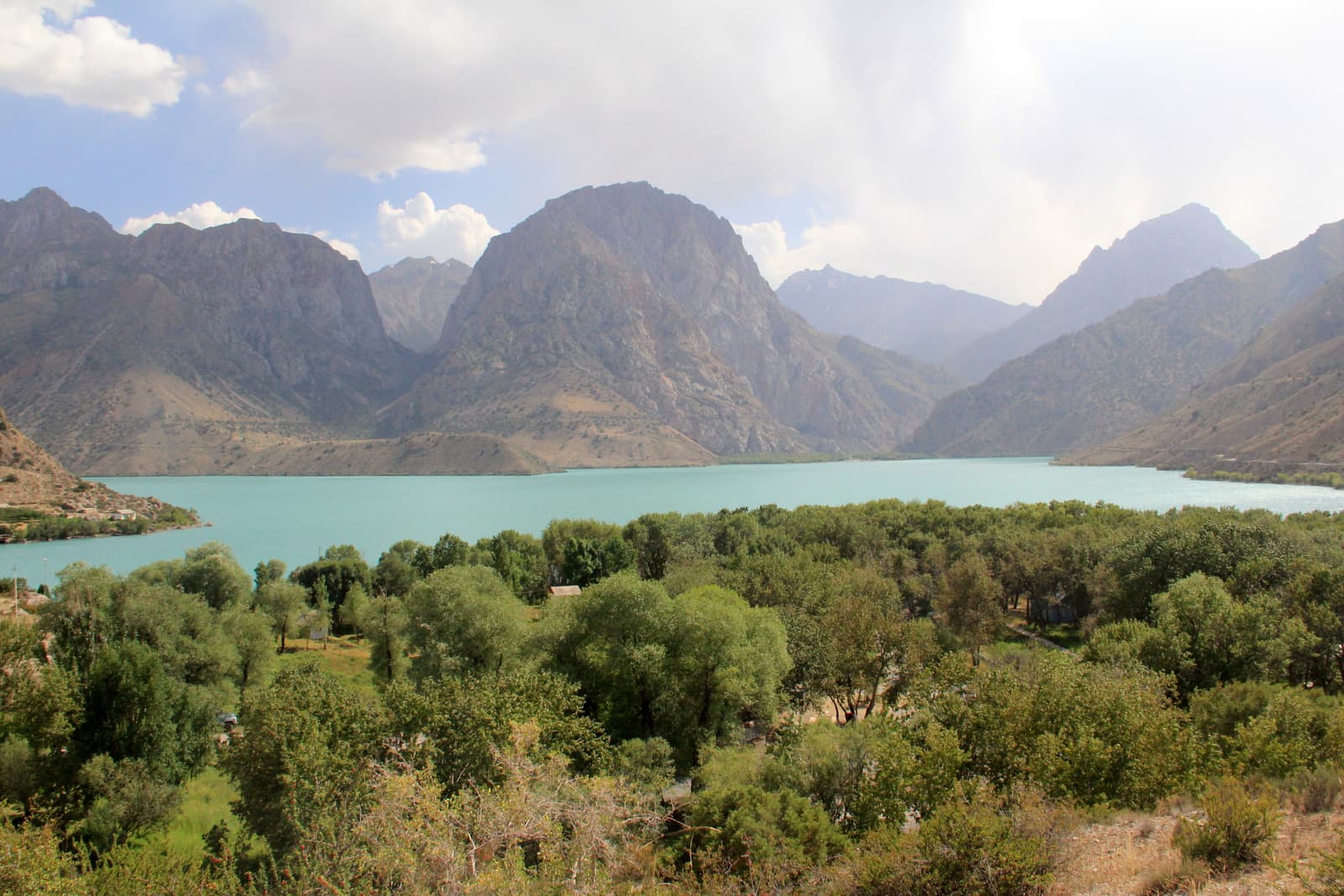 Brilliant turquoise water of Iskanderkul Lake surrounded by forested mountain slopes